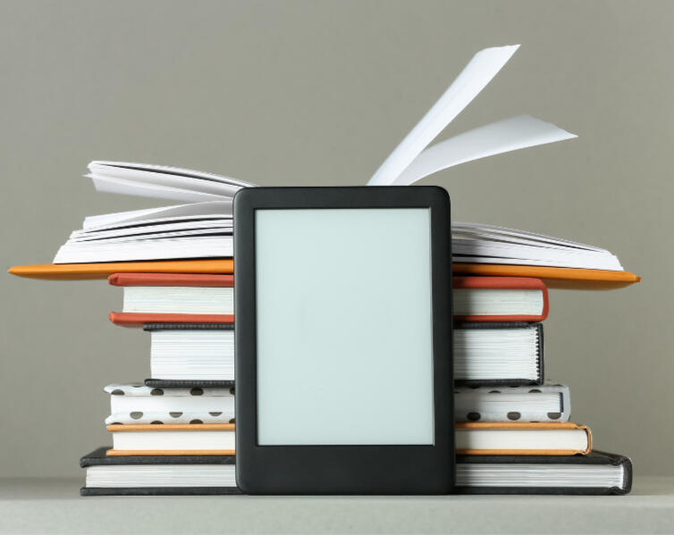 Let's write together. An e-reader sits in front of a stack of books. Representative of writing.